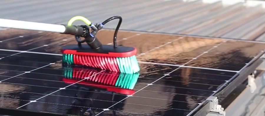 Close-up of a rotating soft brush cleaning dark solar panels with purified water