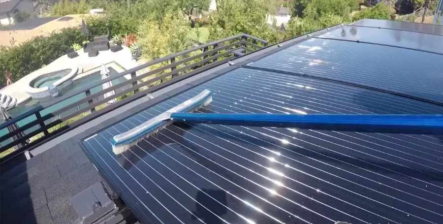 Squeegee on a long pole cleaning black rooftop solar panels beside a backyard pool, solar panel cleaning Henderson NV