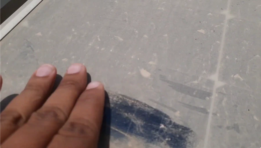 Finger wiped across a dusty solar panel, showing clean glass under the dust