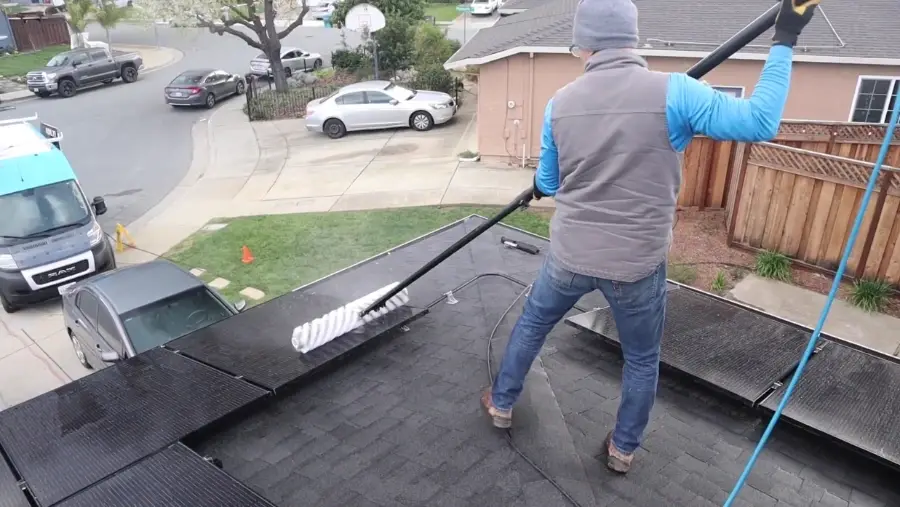 Technician cleaning solar panels on a single-story roof with a water-fed brush pole, solar panel cleaning Spring Valley