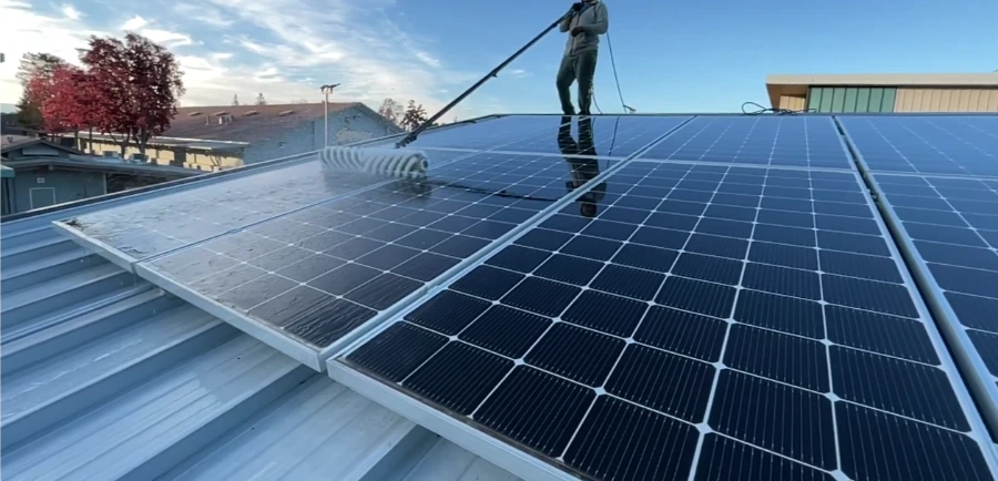 Technician washing a large commercial solar array on a metal roof