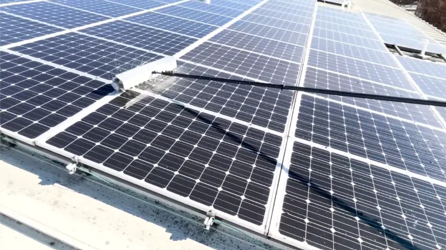 Water-fed brush cleaning rows of panels on a commercial rooftop solar array